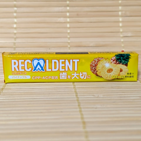 A metallic yellow stick-pack of Recaldent Pineapple sugarless gum displaying pineapple slice artwork on a bamboo mat background.