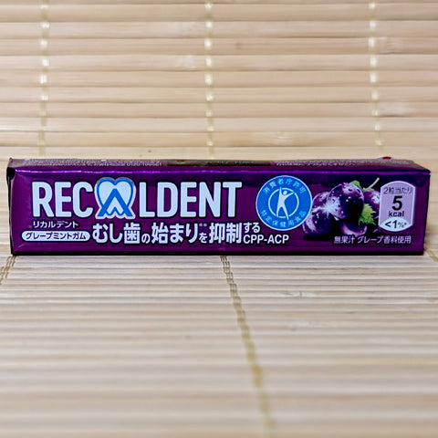 A metallic purple stick-pack of Recaldent Grape Mint sugarless gum displaying dark red grapes and the Tokuho seal on a bamboo mat background.
