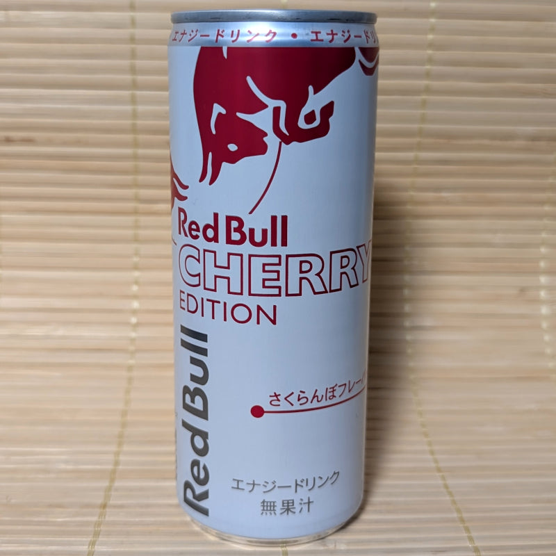 A white and pink 250ml Red Bull can featuring the red bulls logo and Japanese text for Sakuranbo flavor. Displayed on a tatami background.