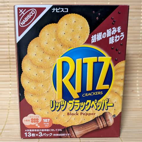 A black and gold Ritz box on a tatami background featuring a wooden pepper grinder, scattered peppercorns, and stacked Ritz crackers.