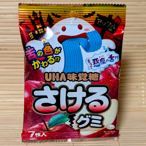 A metallic red 7-piece bag of UHA Mikakuto Sakeru Gummy Halloween Apple featuring a ghost with a blue tongue on a bamboo mat.