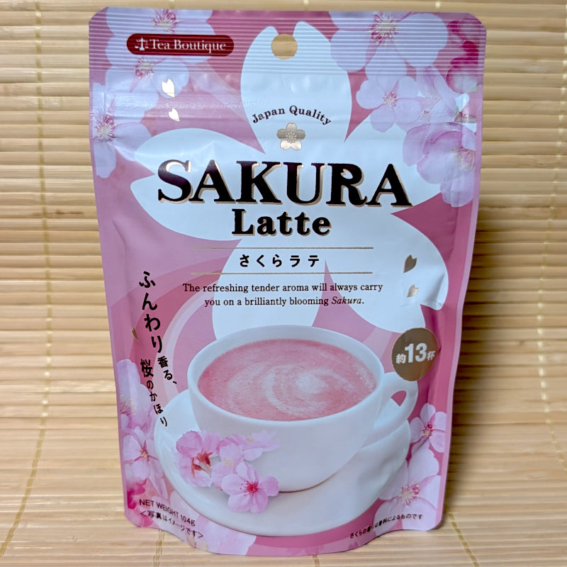 A pink and white Tea Boutique Sakura Latte pouch on a tatami background featuring a cup of pink latte and cherry blossom illustrations.