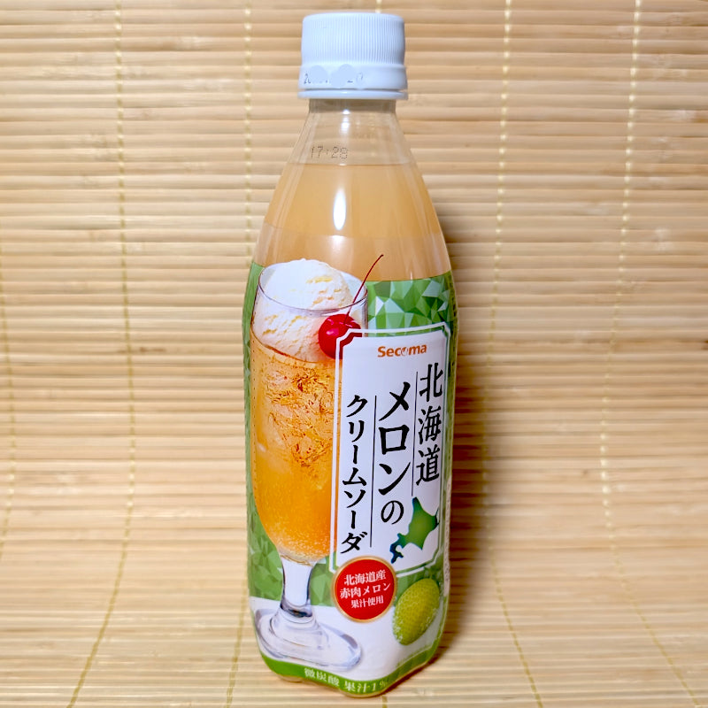 A 500ml plastic PET bottle of Seicoma Hokkaido Melon Cream Soda featuring a cream soda glass graphic with a cherry on a green and white label, on a tatami background.