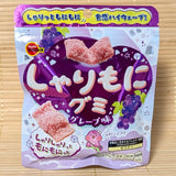 A purple 57g pouch of Bourbon Sharimoni Grape Gummies showing crunchy sugar coated gummies on a bamboo mat background.