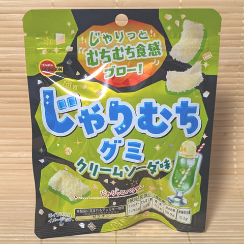A green and black 61g pouch of Bourbon Jyarimuchi Gummy Cream Soda showing melon soda float graphics on a bamboo background.   