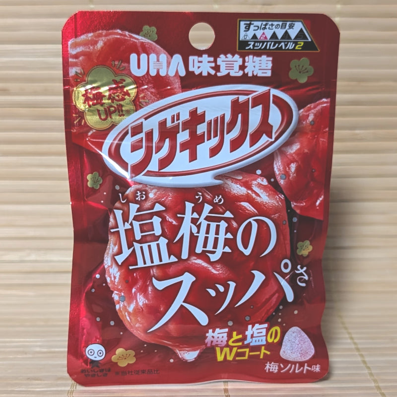 A metallic red 20g pouch of UHA Shigekix Salty Sour Ume Plum gummies showing a Level 2 sourness meter, pickled ume illustrations, and a cone-shaped gummy on a bamboo mat background.