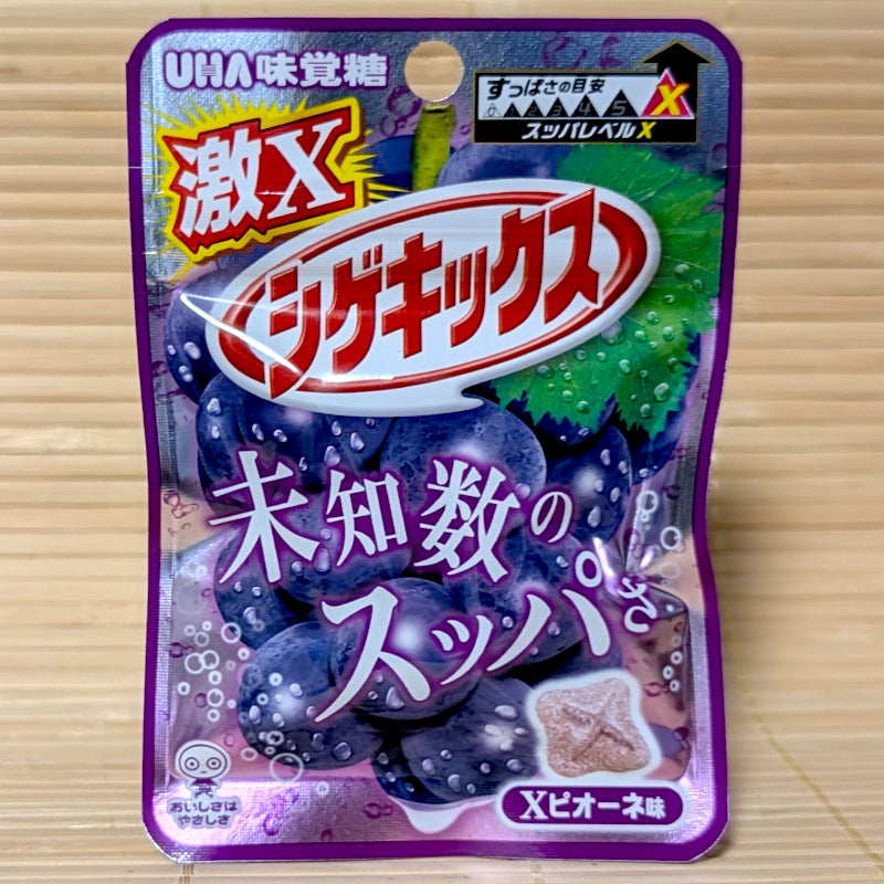 A metallic purple mini pouch of UHA Shigekix Geki X candy showing large dark purple wine grapes and an X-stamped brown sour button disc on a tatami background.