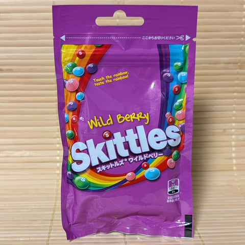 A purple resealable Skittles bag on a tatami background featuring rainbow graphics and colorful Wild Berry candy pieces.