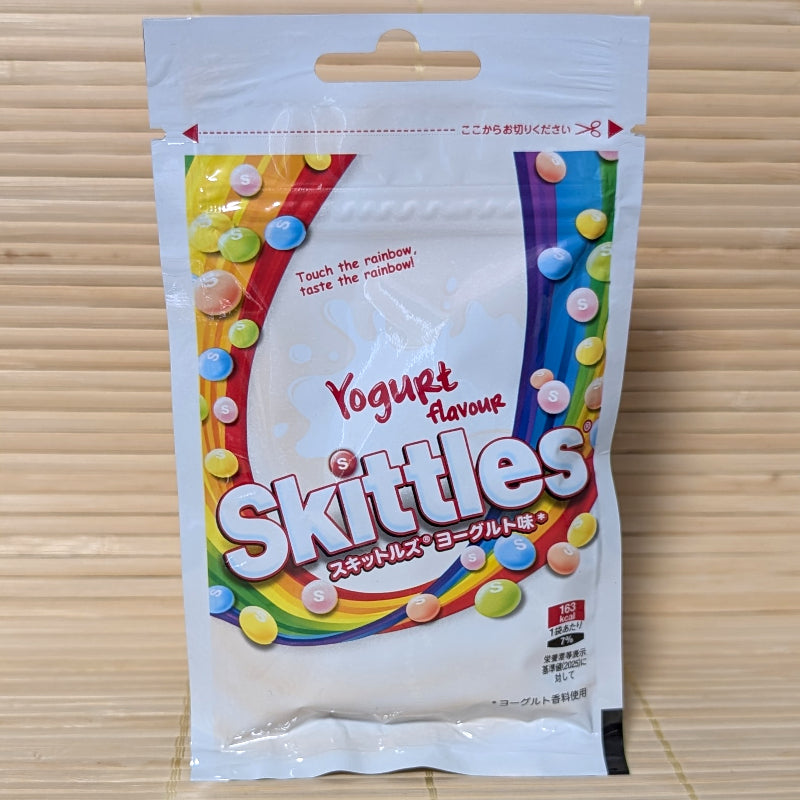 A white and rainbow-themed resealable Skittles pouch on a tatami background featuring yogurt-swirled "S" candies and various creamy flavors.