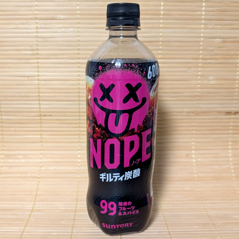 A black 600ml bottle of Suntory NOPE soda with a large neon pink graffiti-style smiley face on the label. Displayed on a tatami surface.