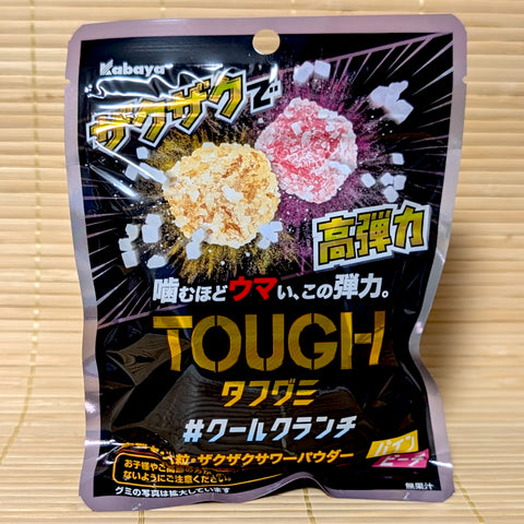 A metallic purple and black resealable pouch of Kabaya TOUGH Gummy Cool Crunch showing crystal-coated yellow pineapple and pink peach candy cubes on a tatami background.