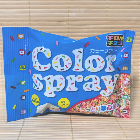 A bright blue Tirol Chocolate bag on a tatami background with "Color Spray" in large bubble letters and a cross-section showing sprinkles.