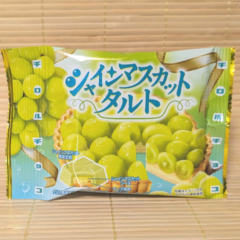 A bright green and white mini pouch of Tirol Shine Muscat Tart chocolate showing a fresh grape tart illustration and a cube cross-section on a tatami background.