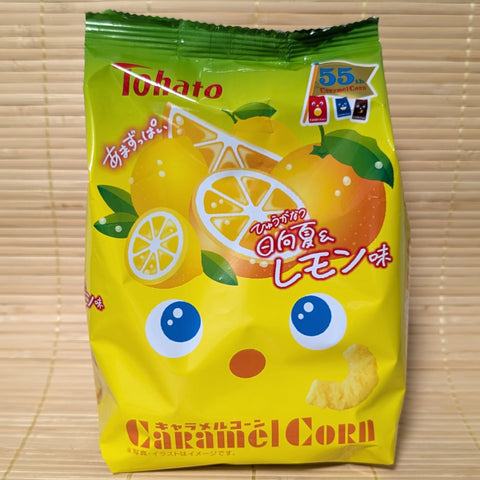 A bright yellow bag of Tohato Caramel Corn with lemon and Hyuganatsu graphics and a 55th-anniversary logo, on a Japanese tatami background.