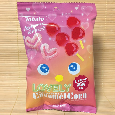 A pink and orange gradient Tohato Caramel Corn bag on a tatami background featuring heart-shaped snacks and candied strawberry skewers.