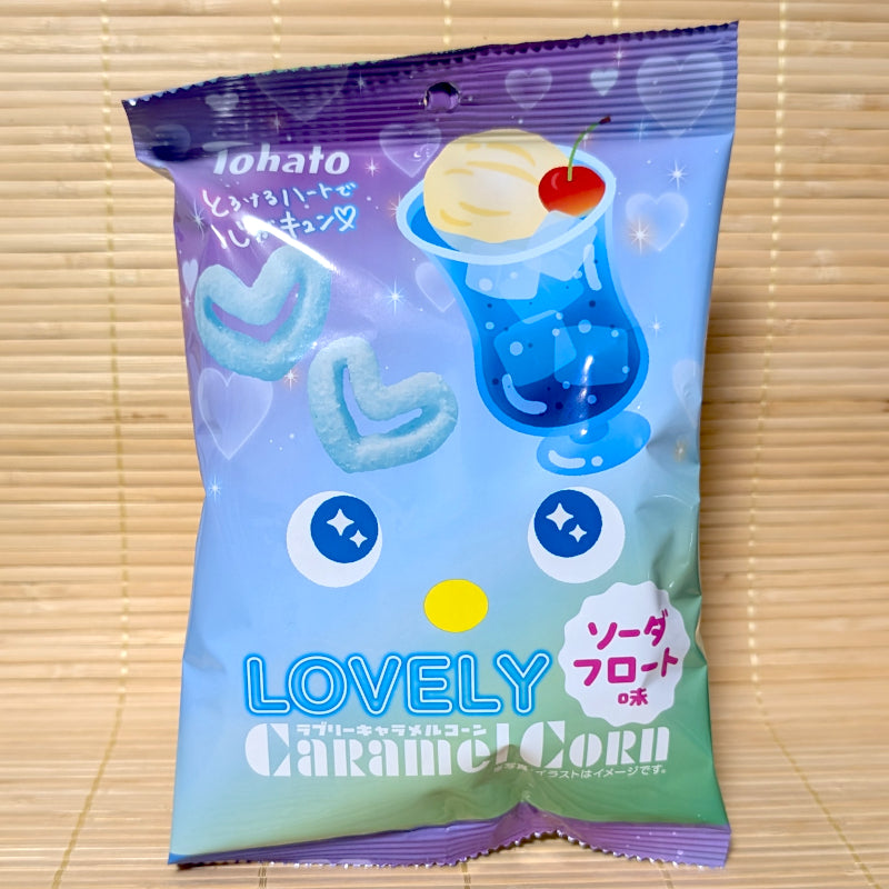 A pastel blue and purple 43g bag of Tohato Lovely Caramel Corn Soda Float showing a blue soda float illustration and two light blue heart shaped puffs on a bamboo background.