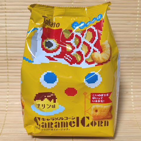 A bright yellow bag of Tohato Caramel Corn with pixel-art blue eyes, a custard pudding illustration, and a red koinobori carp streamer.