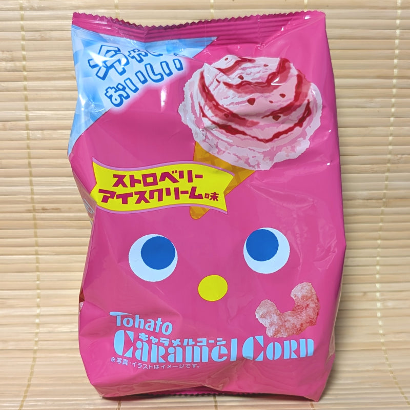A hot pink bag of Tohato Caramel Corn Strawberry Ice Cream showing a cartoon face and a strawberry waffle cone graphic on a tatami background.