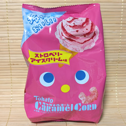 A hot pink bag of Tohato Caramel Corn Strawberry Ice Cream showing a cartoon face and a strawberry waffle cone graphic on a tatami background.