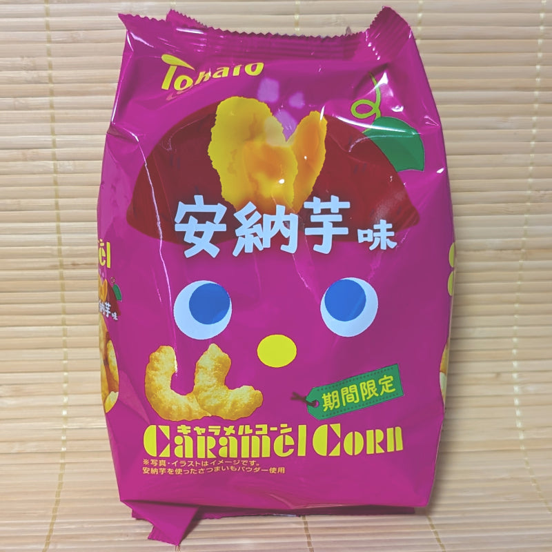 A bright magenta bag of Tohato Caramel Corn Anno Imo Sweet Potato displaying cute character eyes and sweet potato artwork on a bamboo mat background.