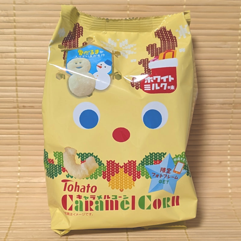 A yellow winter-themed 62g bag of Tohato Caramel Corn White Milk Flavor showing snowman graphics on a bamboo background.   