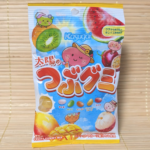 A bright blue Tsubugumi bag on a tatami background featuring tropical fruit mascots and colorful bean shaped gummies.