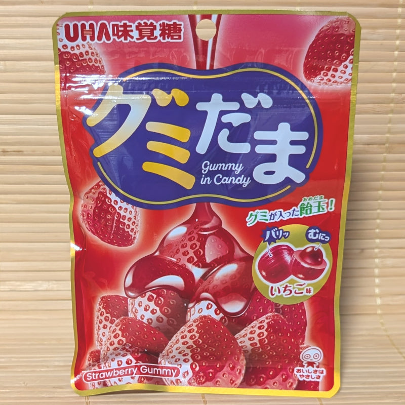 A bright red pouch of UHA Gumidama featuring fresh strawberries and a cross-section illustration of the candy shell and gummy core.