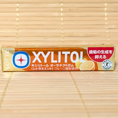 A gold and orange pack of Xylitol Oral Protect Citrus Mint Chewing Gum showing citrus fruit graphics and the Tokuho seal on a bamboo background.   