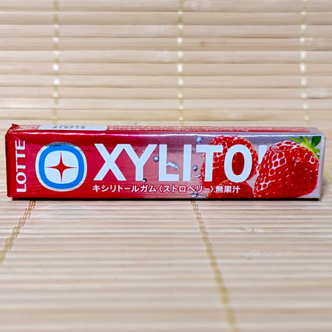 A metallic red and silver stick of Lotte Xylitol Strawberry chewing gum showing fresh strawberry graphics on a tatami background.
